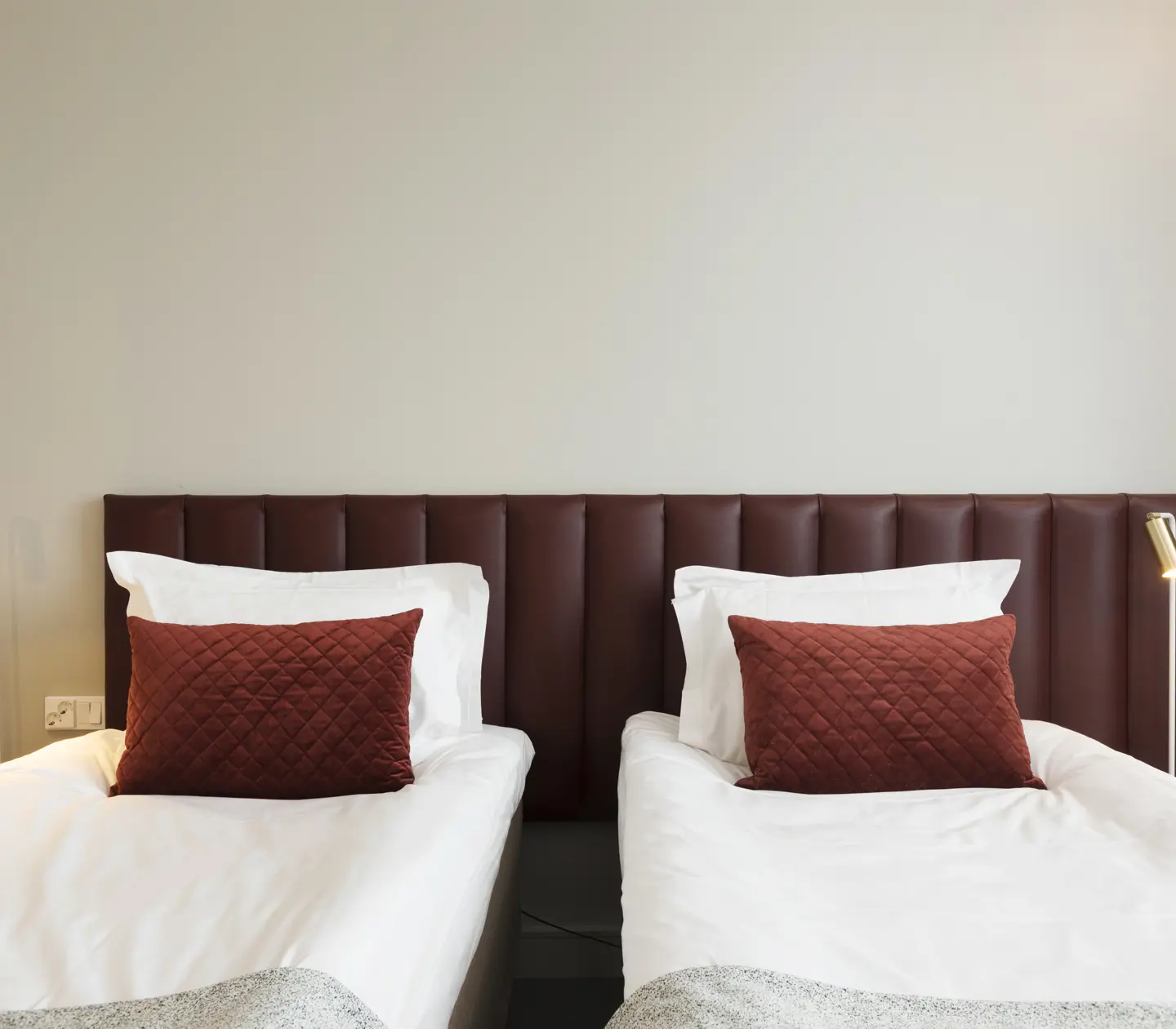 Bright hotel room with two single beds next to each other, burgundy headboard and small bedside lamps