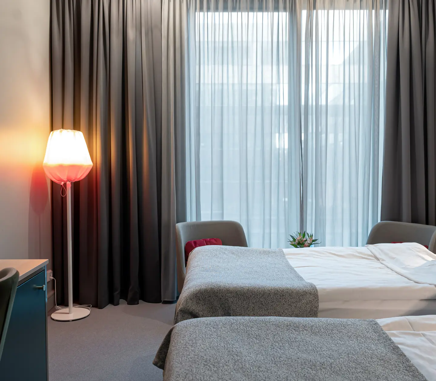 Bright hotel room with two single beds next to each other, desk and window