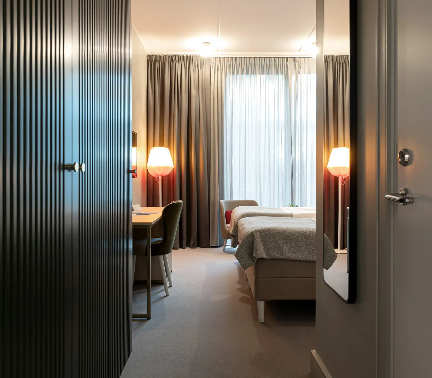 Bright hotel room with two single beds next to each other, desk and wardrobe