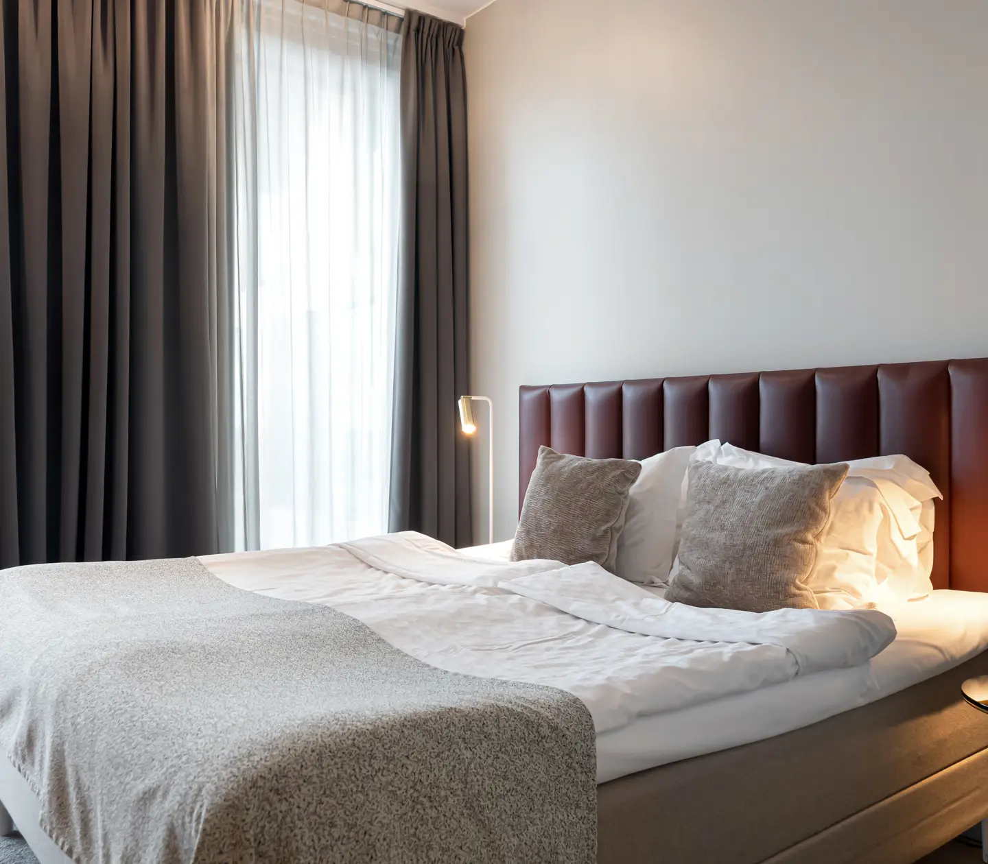 Bright hotel room with bed, burgundy headboard and window