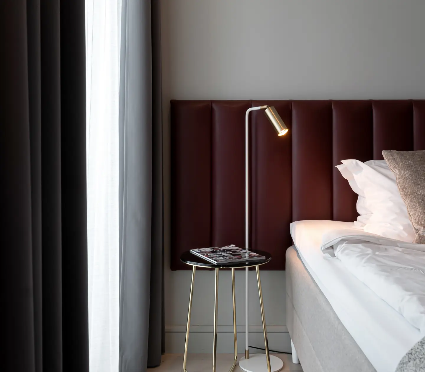 Bright hotel room with bed, burgundy headboard and small bedside lamp