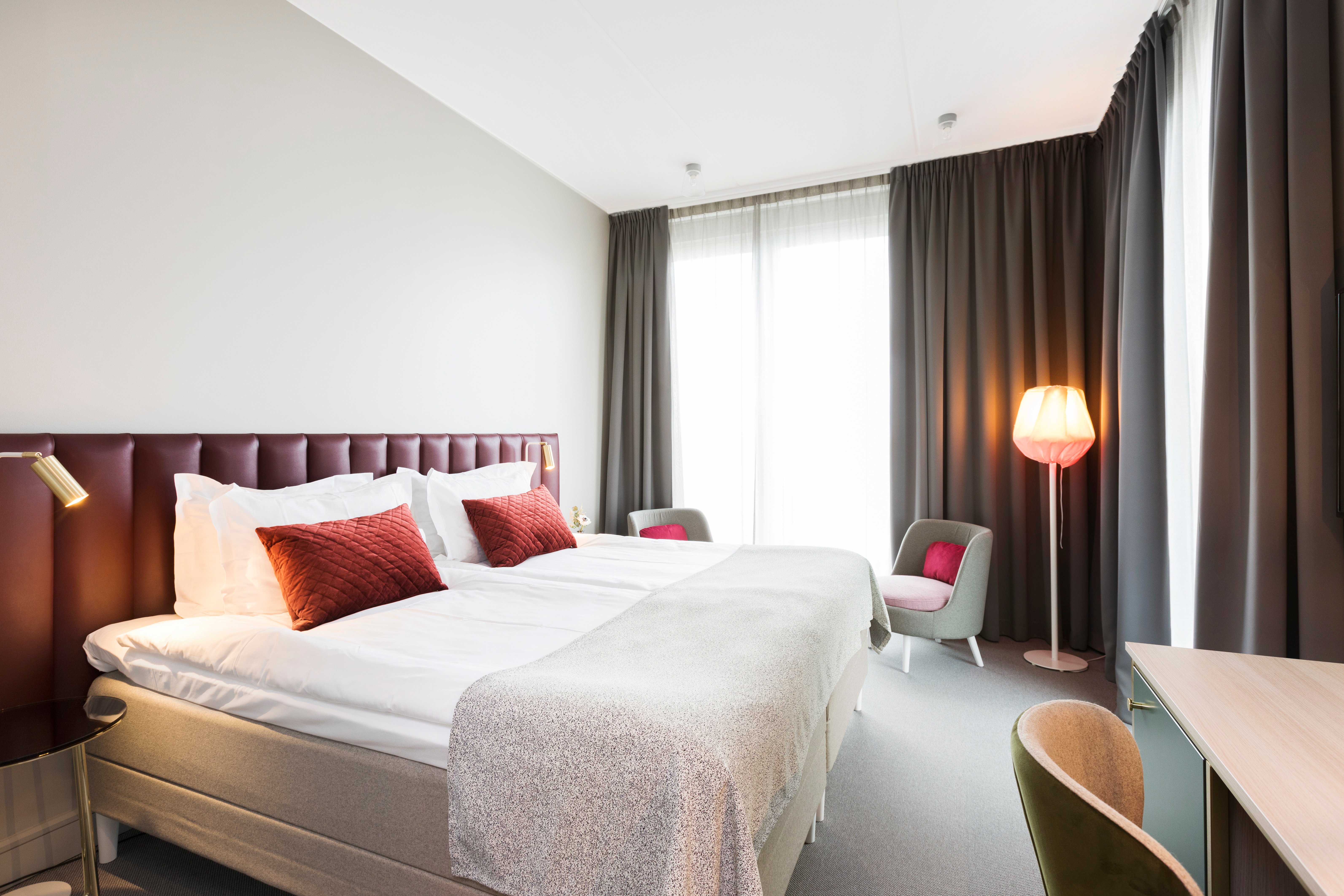 Ljust hotellrum med säng, vinröd sänggavel och stort fönster