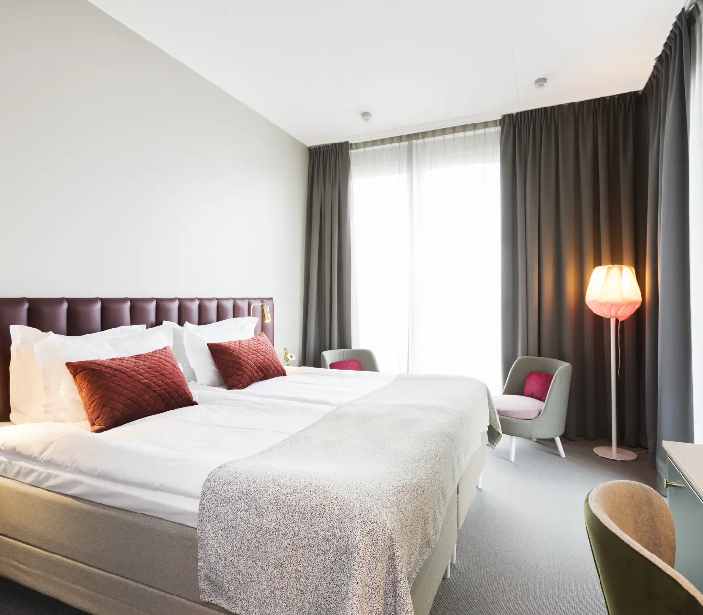 Bright hotel room with bed, burgundy headboard and large window