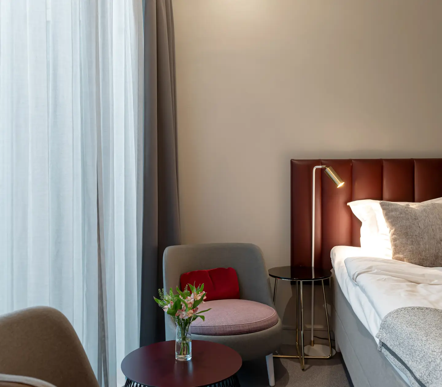 Bright hotel room with bed, burgundy headboard and armchairs