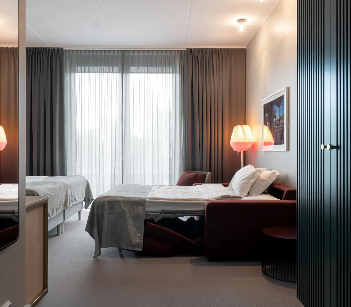 Bright hotel room with wardrobe, sofa bed and large window