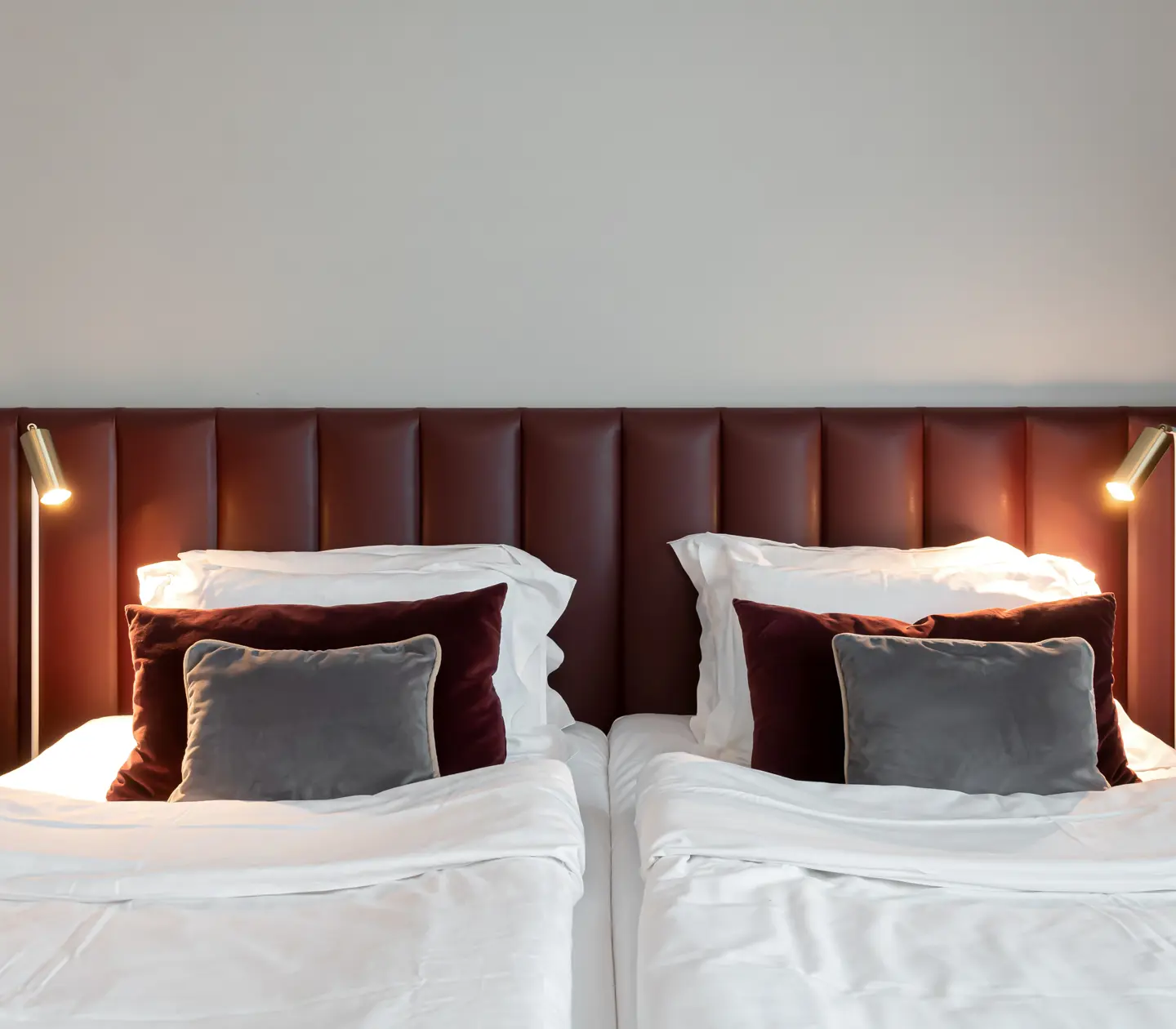 Bright hotel room with bed, burgundy headboard and gray pillows