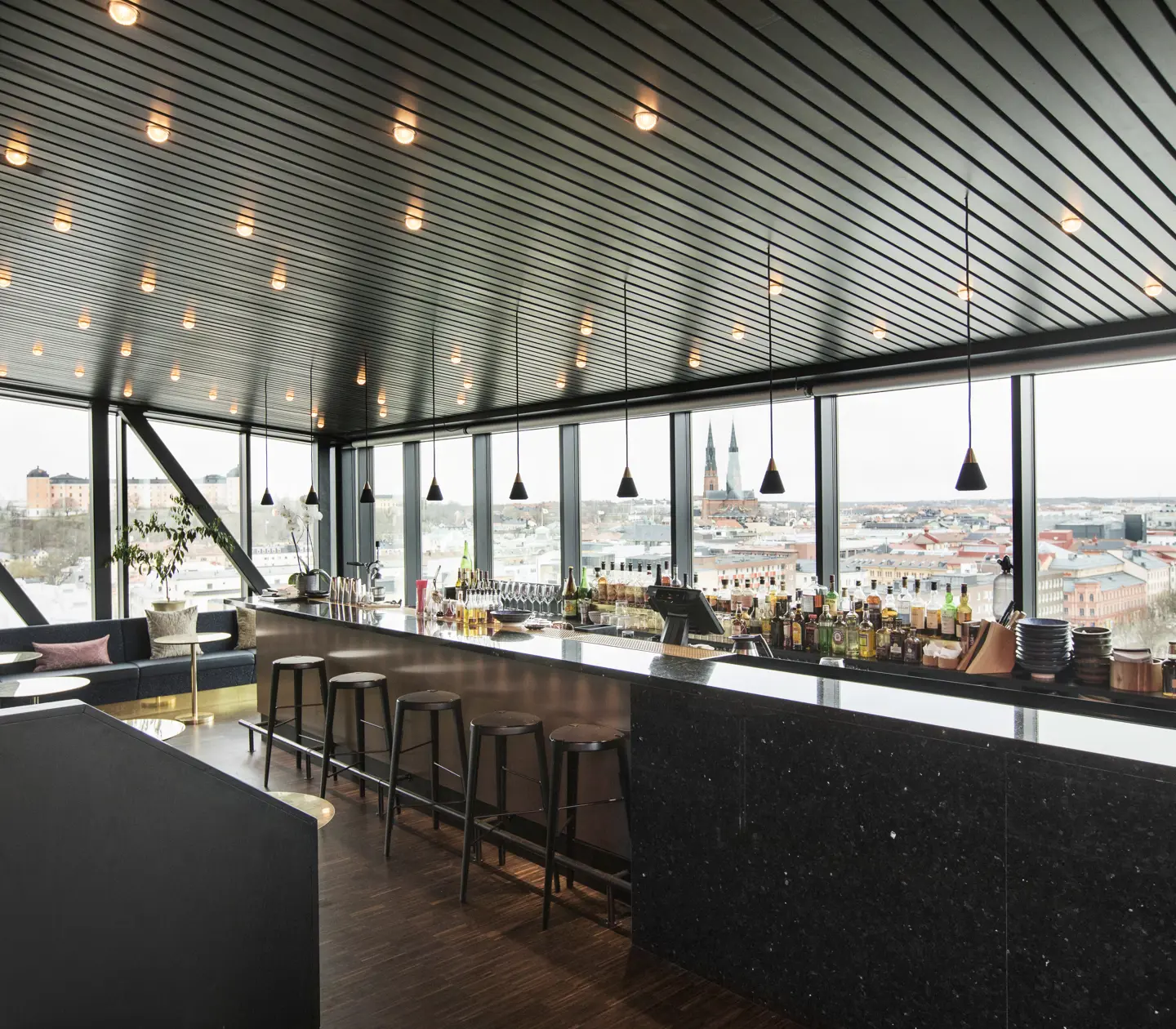 Restaurant environment with a large bar, ceiling lights and windows along the walls with a view of Uppsala