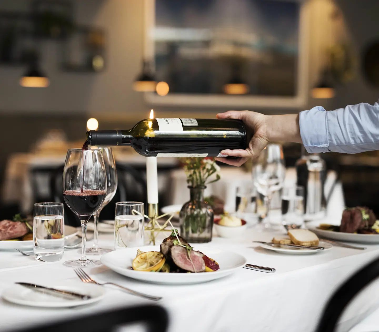 Dinner served for four with food on the plates and red wine poured into wine glasses