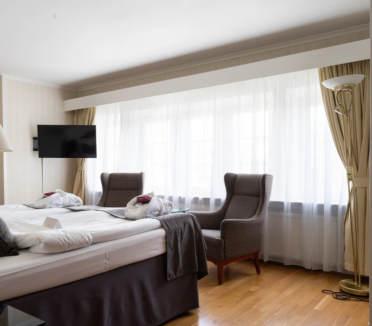 Mysigt hotellrum med morgonrock på säng, fåtölj och fönster