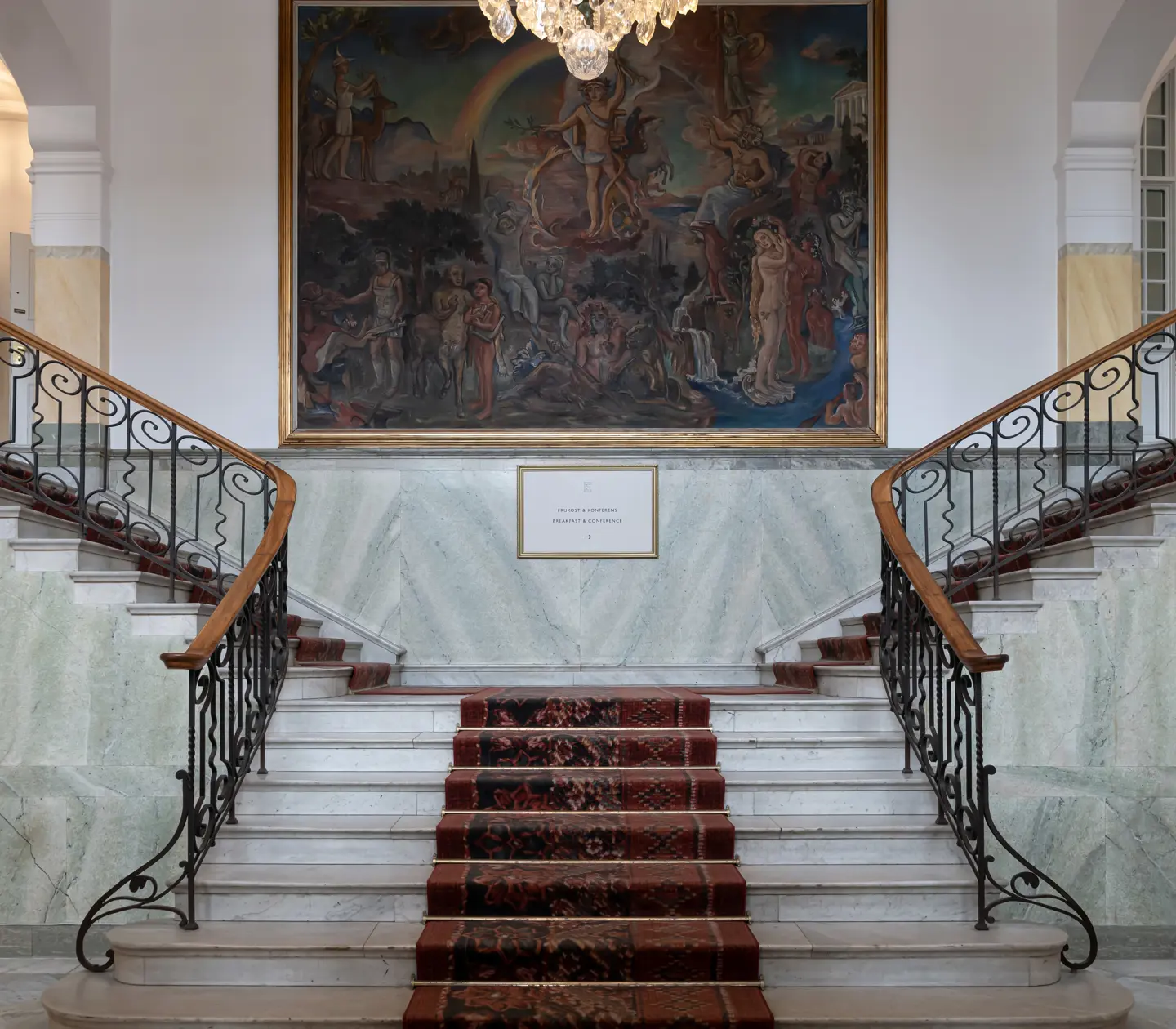 Fancy stone staircase with carpets, railings and large central painting