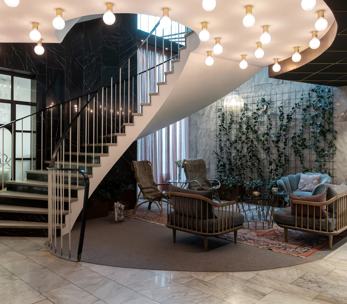 Hotel lobby with lounge furniture, plants along the walls and staircase with ceiling lights
