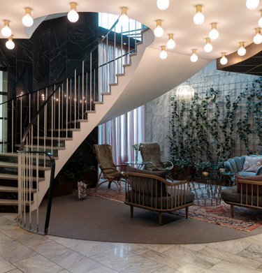 Hotellobby med loungemöbler, växter längs väggarna och trapp med taklampor