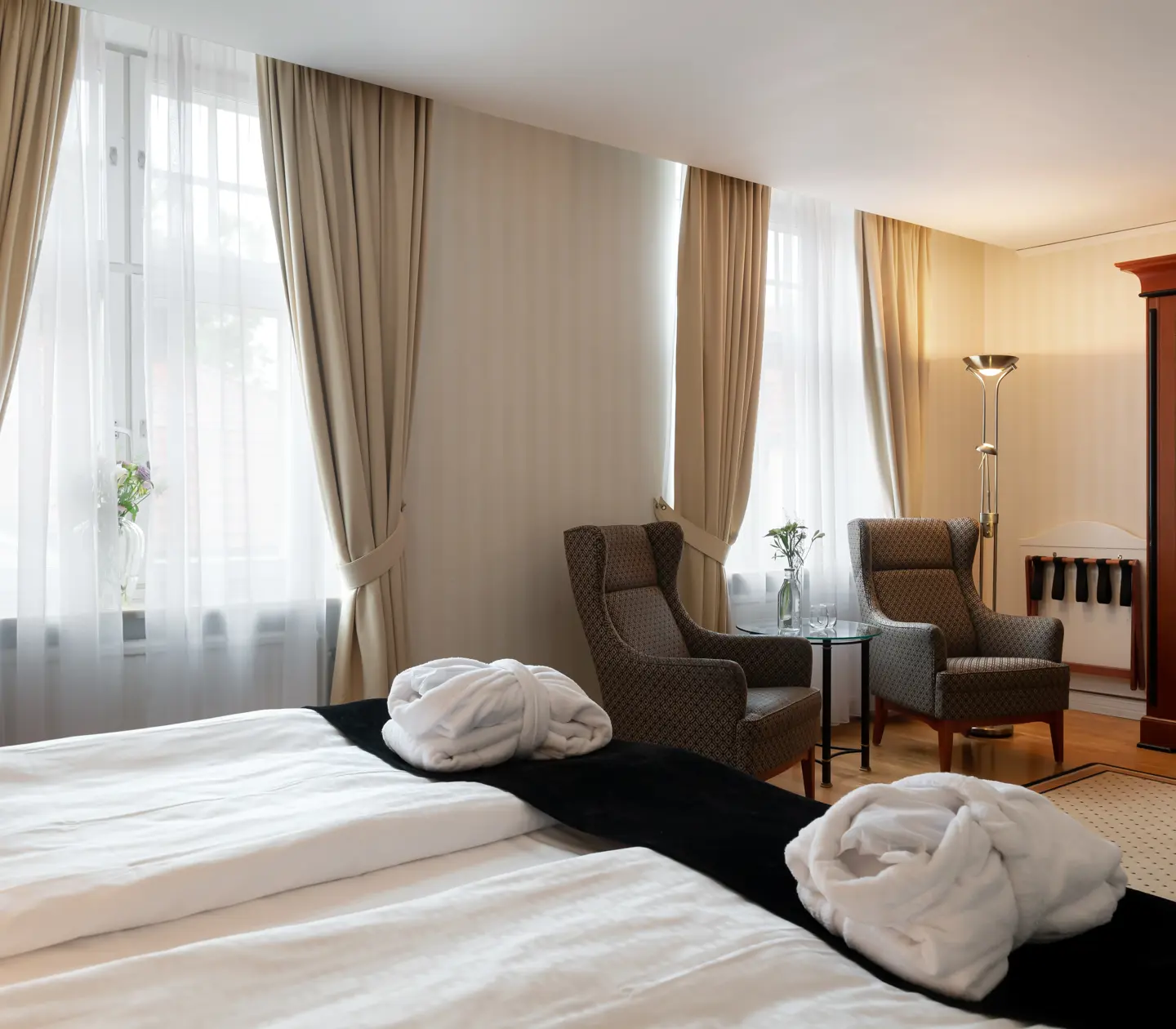 Large hotel room with bathrobes on bed, armchairs and window
