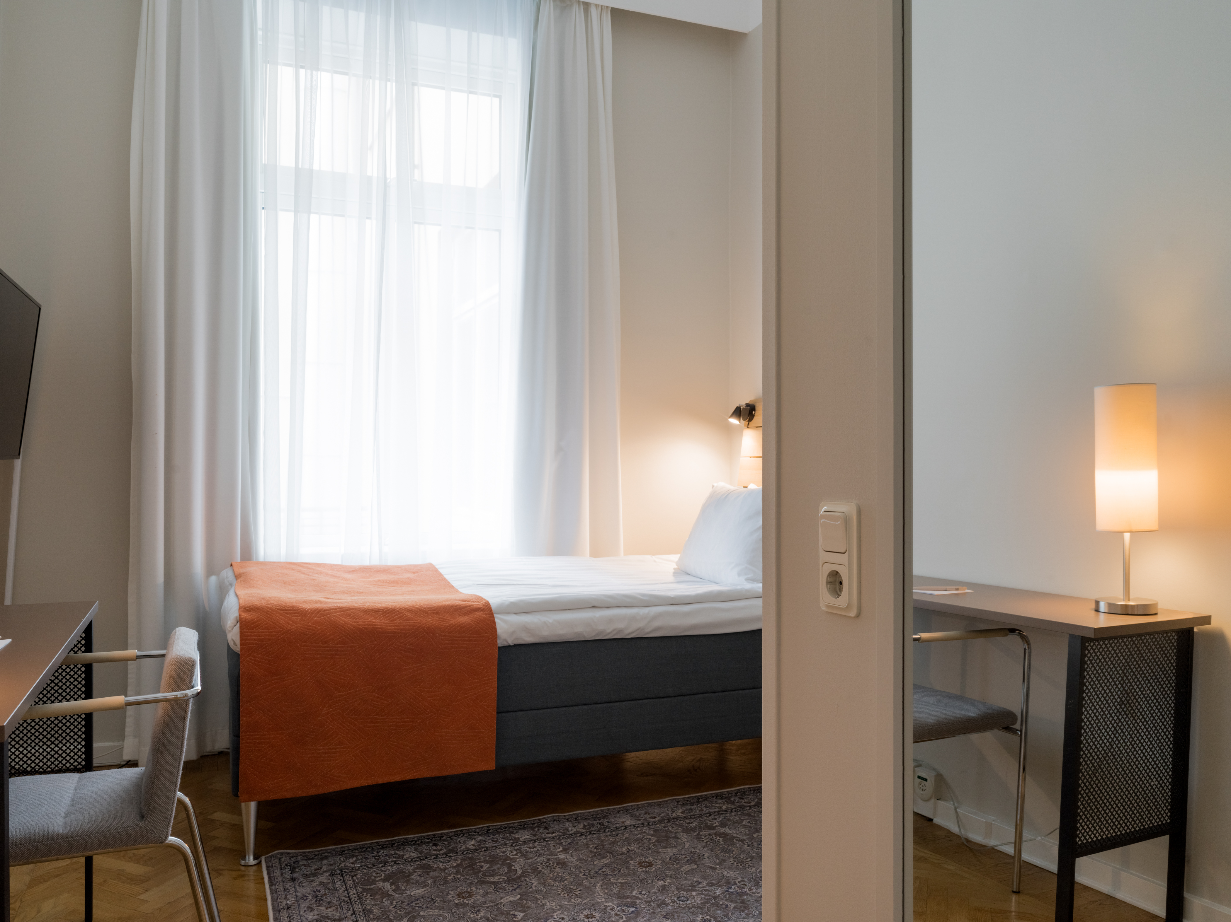 Mysigt hotellrum med enkelsäng, skrivbord och fönster