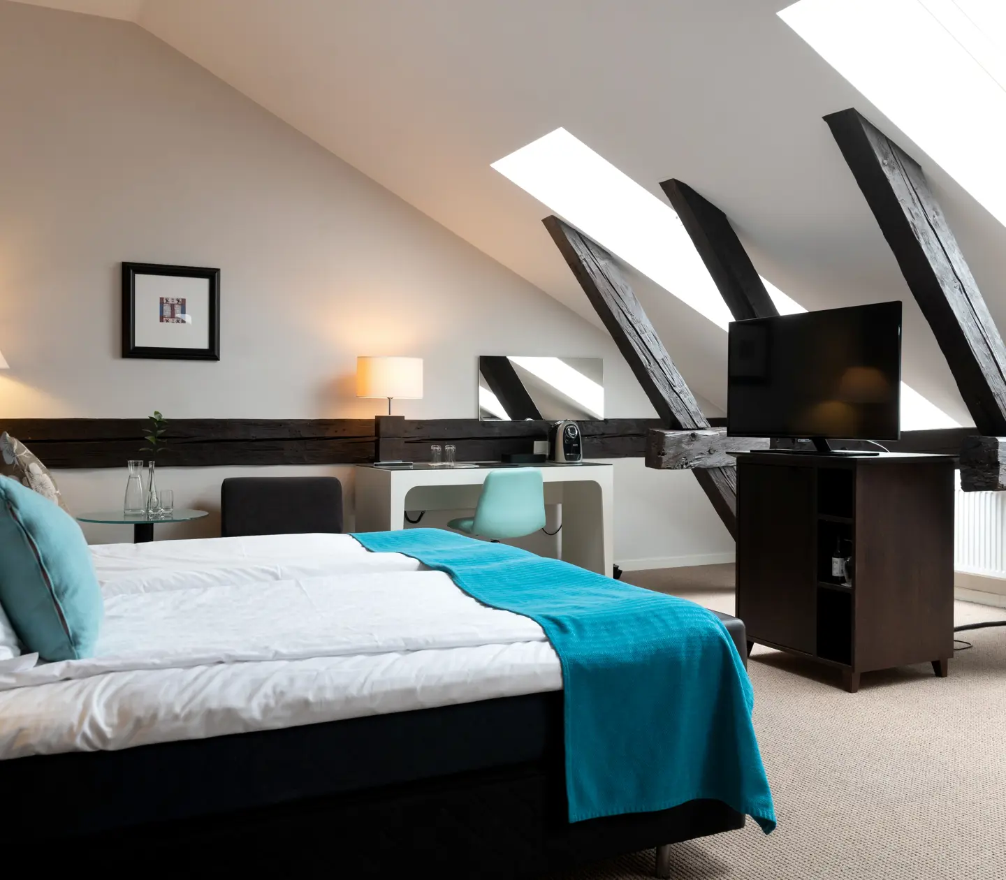 Hotel room with wooden beams, slanted ceiling, double bed and desk