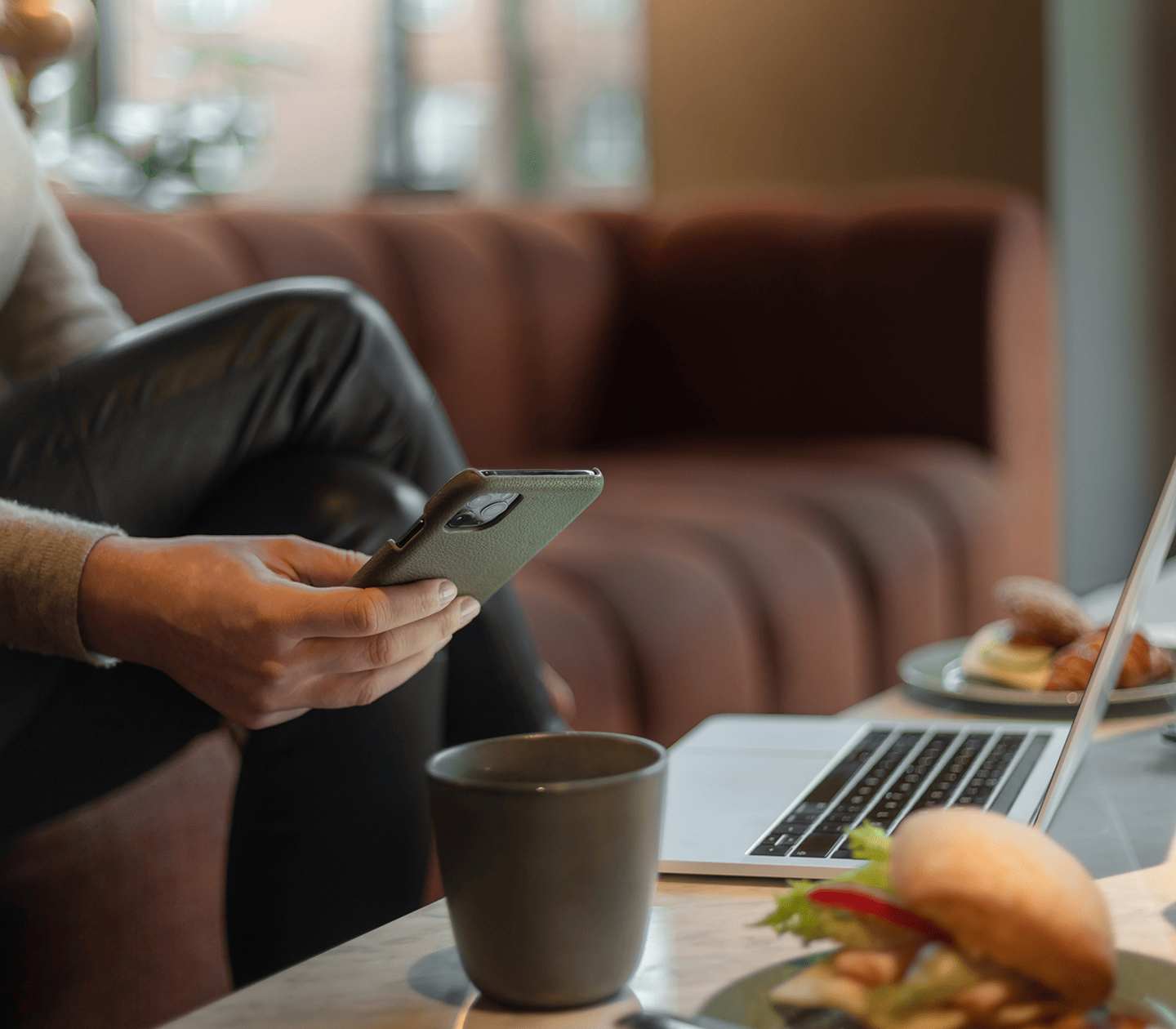 A guest having coffee on a couch while using their computer