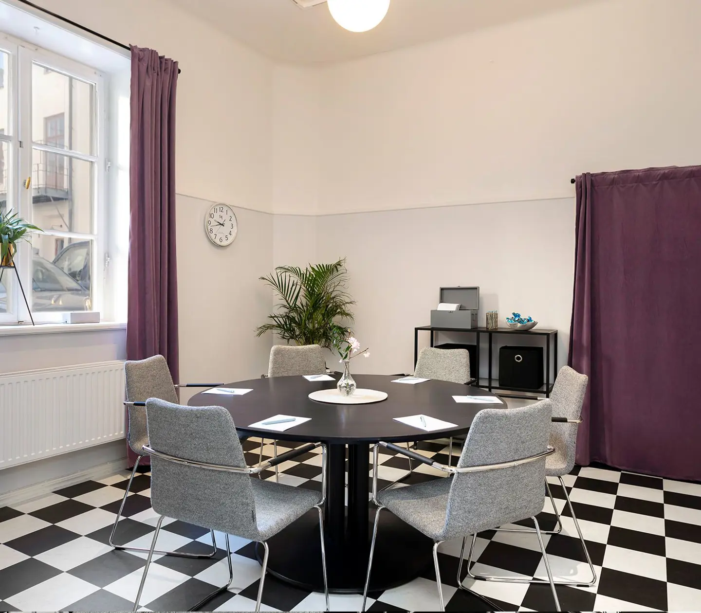 Konferensrum med schackrutigt golv, runt bord och stort fönster