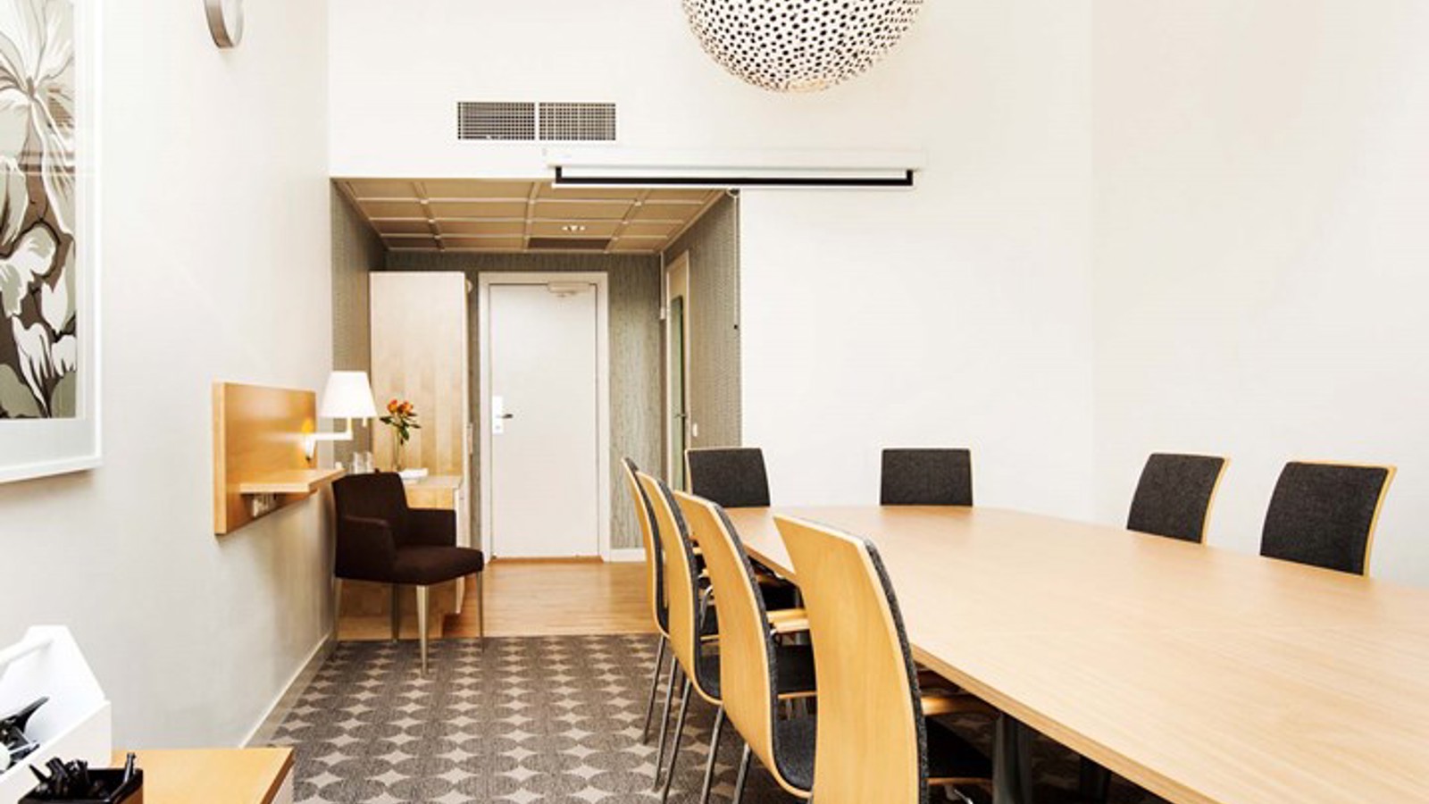 Konferensrum med styrelsesittning, träbord, gråmönstrad matta, vita väggar