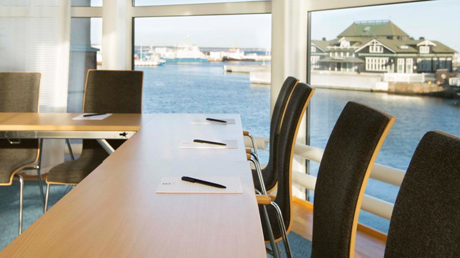 Konferensrum med träbord, mörka stolar, stora fönster med havsutsikt