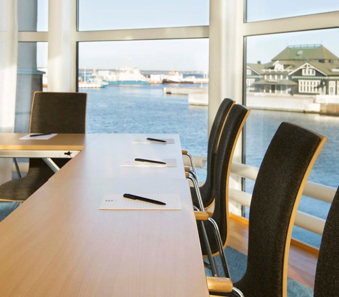 Konferensrum med träbord, mörka stolar, stora fönster med havsutsikt