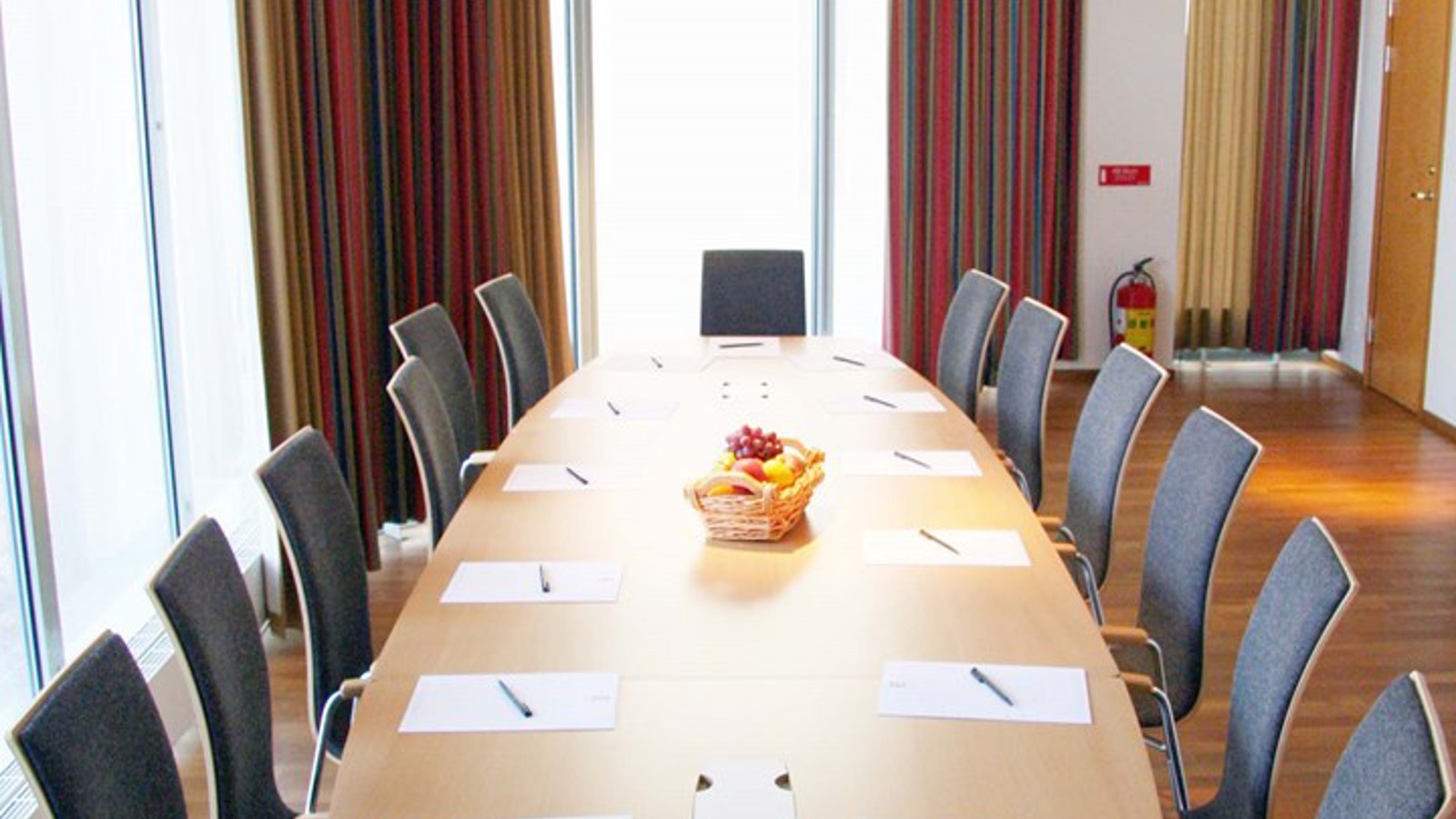 Konferensrum med styrelsesittning, träbord, stora fönster och färgglada gardiner
