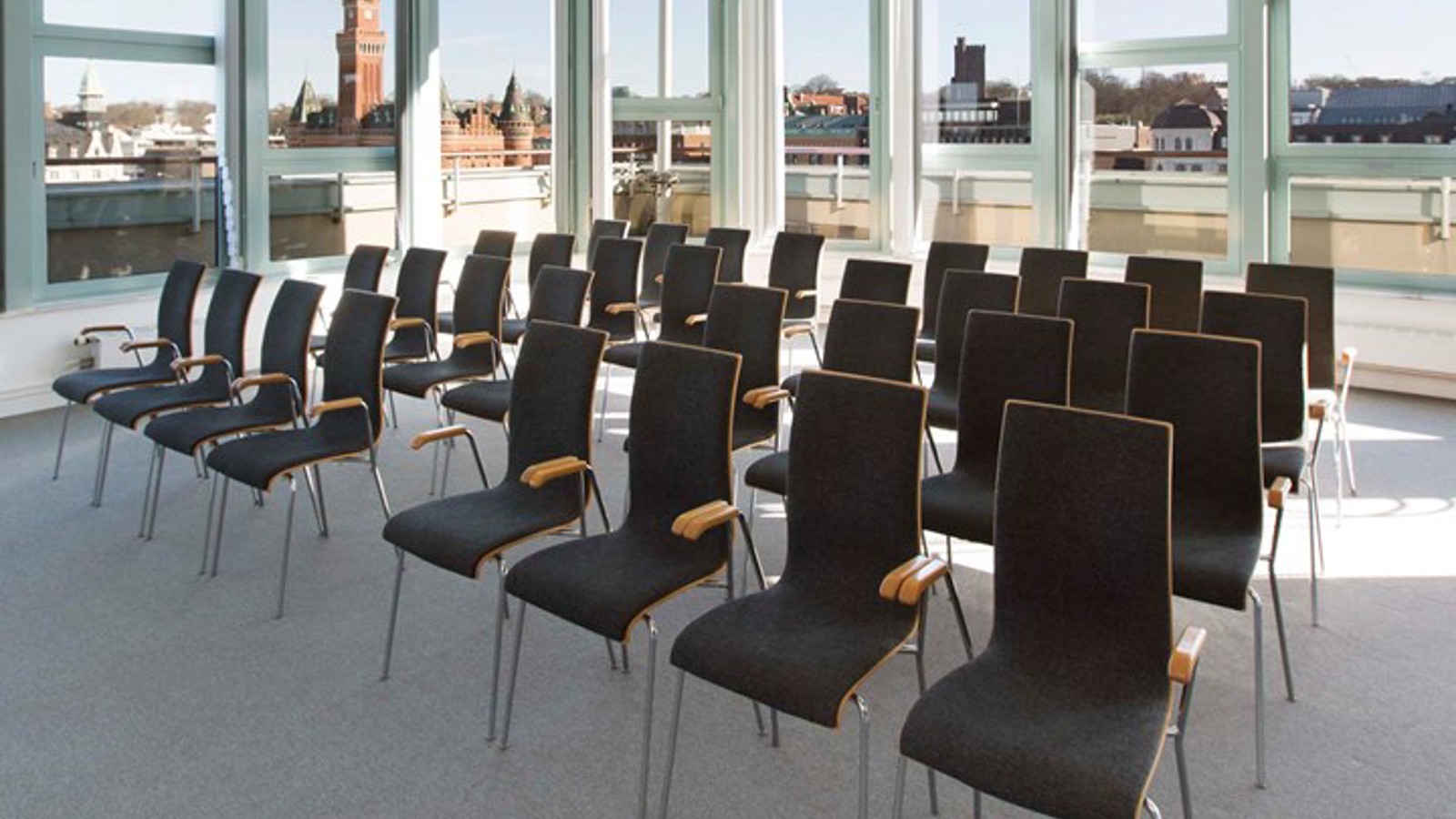 Konferensrum med biosittning, svarta stolar, grå matta och stora fönster med utsikt