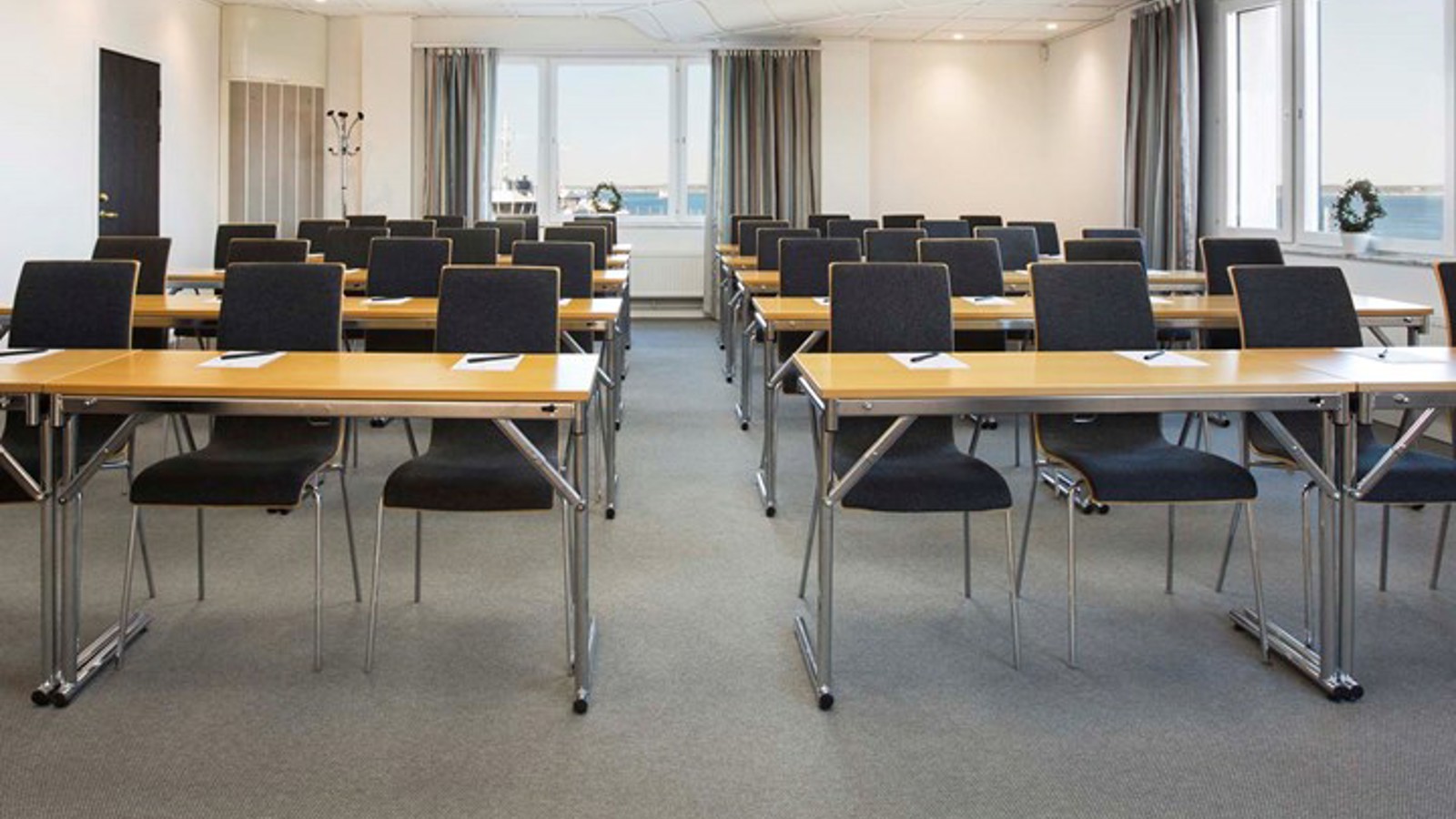 Konferensrum med skolsittning, träbord, svarta stolar och stora fönster med havsutsikt