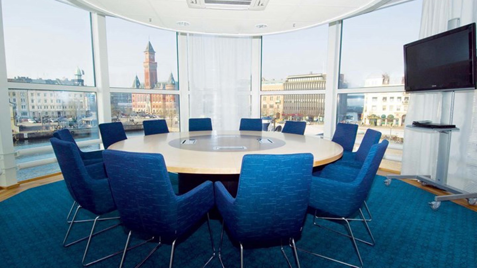 Konferensrum med runt bord, blå fåtöljer, blå matta och stora fönster med utsikt