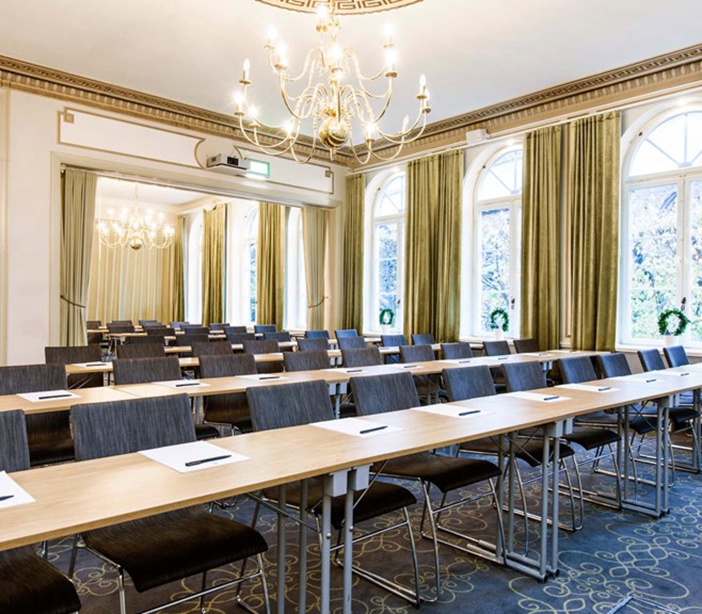 Konferensrum med skolsittning, gulddetaljer, stora fönster och blå matta