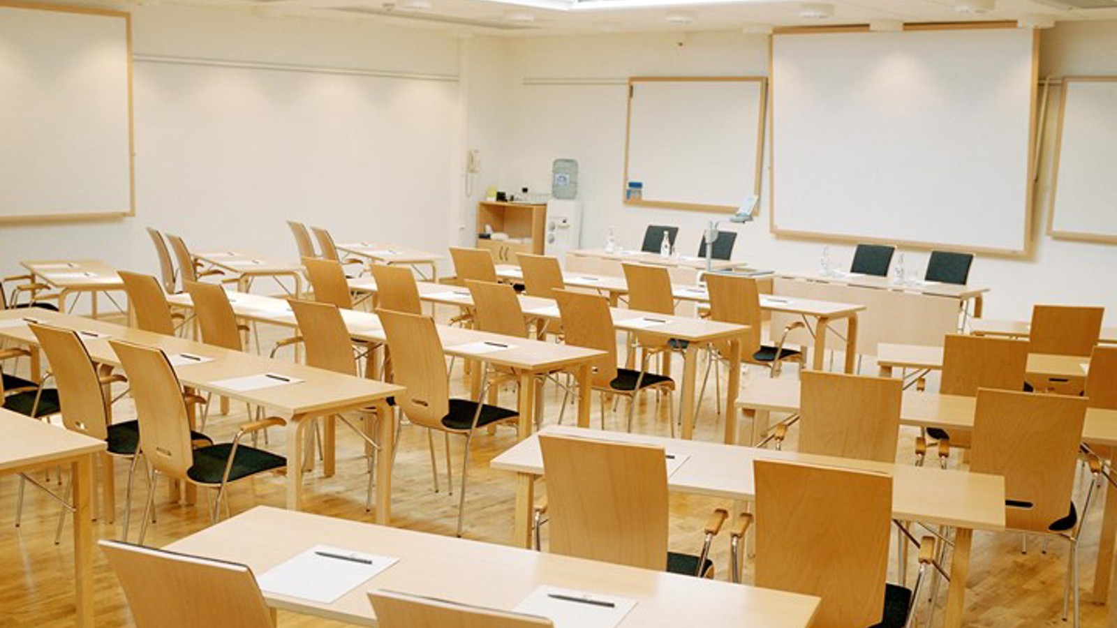 Konferensrum med skolsittning, vita väggar, träfärgade bord och stolar