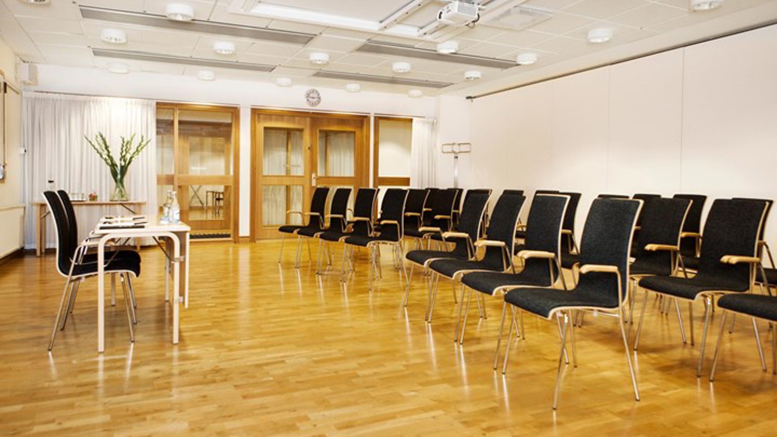 Konferesrum med biosittning, vita väggar, parkett, svarta stolar