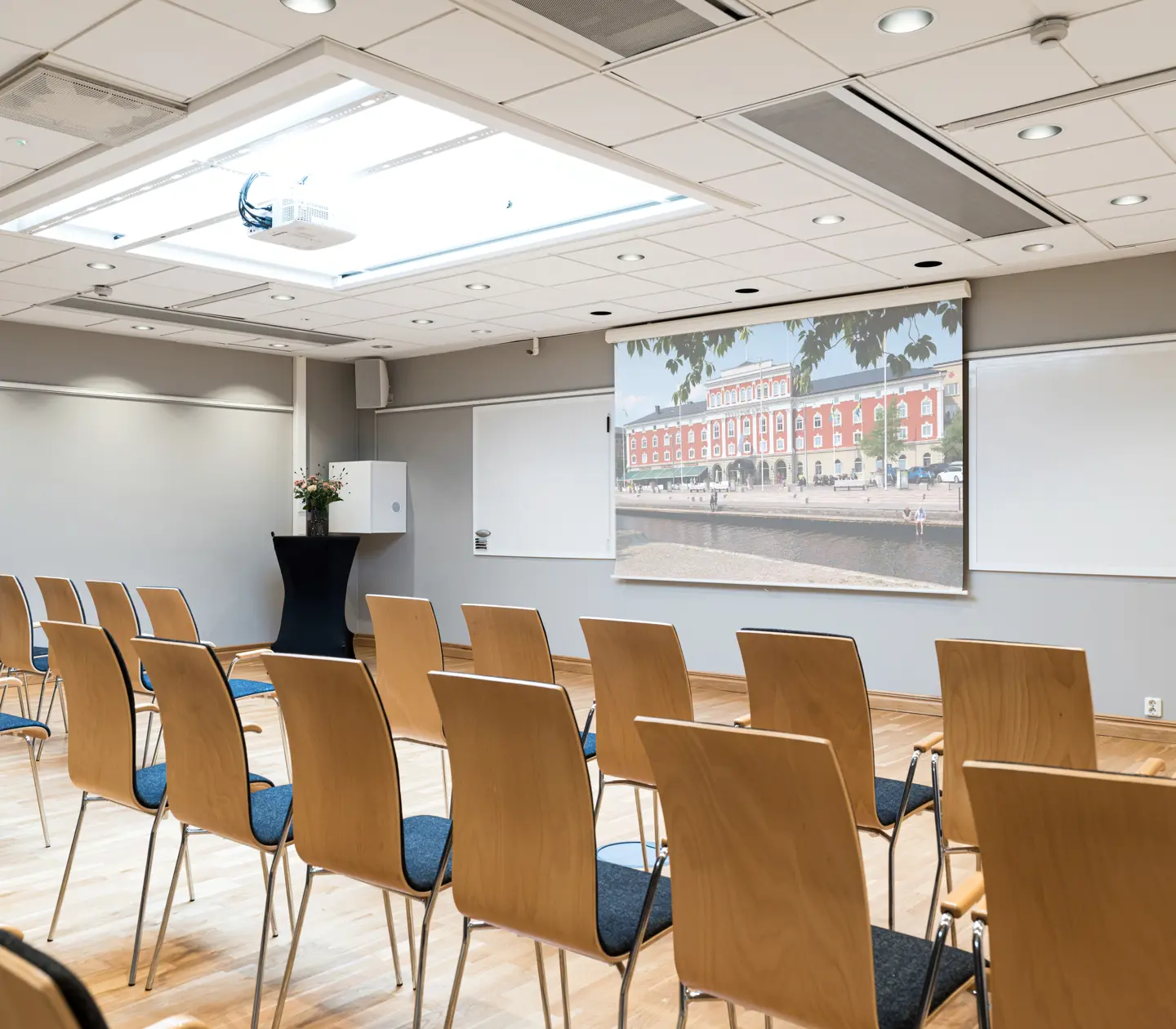 Modern konferenslokal med trästolar, projektor och stor bildskärm, redo för presentation eller möte.