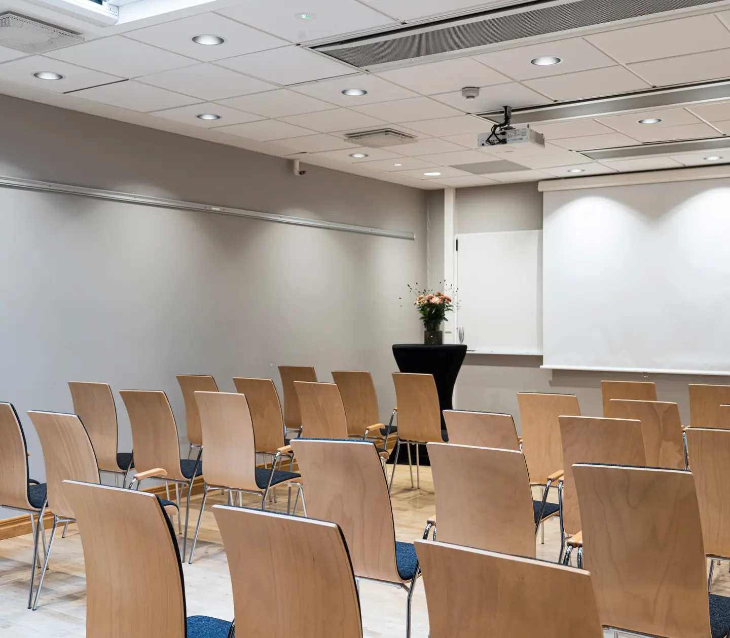Konferensrum med trästolar och projektorduk, redo för presentation eller möte.