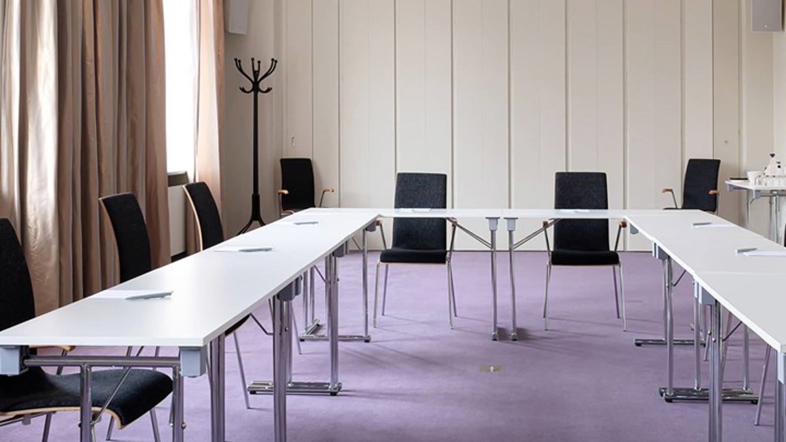 Konferensrum med u-sittning, vita bord och lila matta
