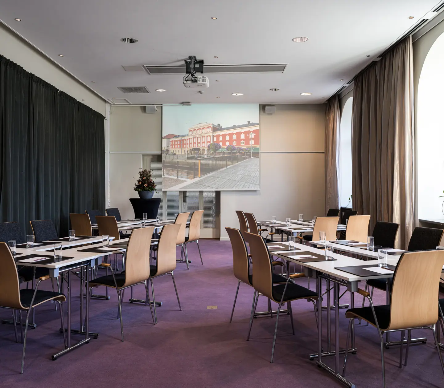 Moderna möteslokaler med fönster och skrivbord uppställda i en u-formad design, perfekt för konferenser och affärsmöten.