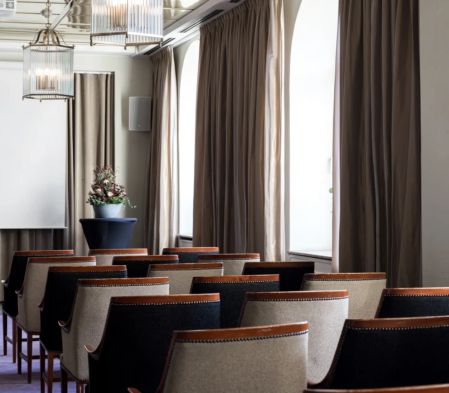 Elegant konferensrum med rad av stolar, projektorduk och stora fönster med gardiner.