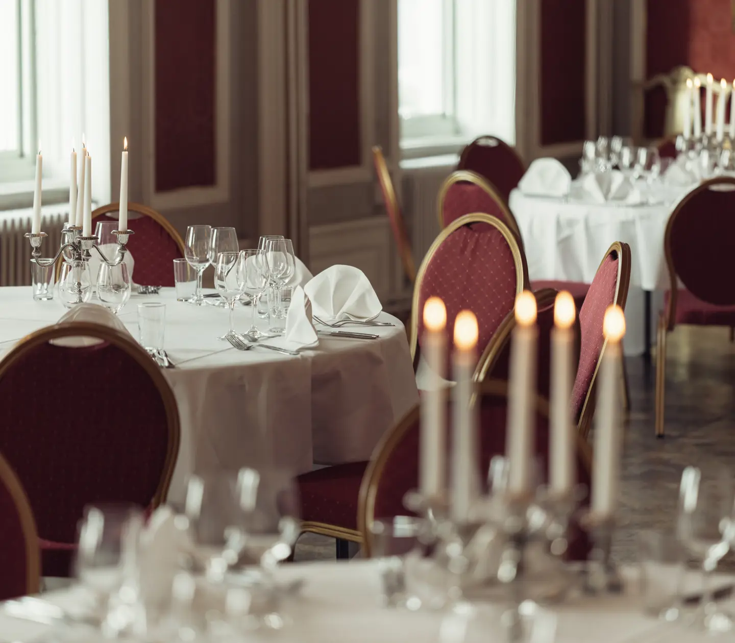 Elegant dukning med vita dukar, röda stolar och tända ljus i en fin restaurangmiljö.