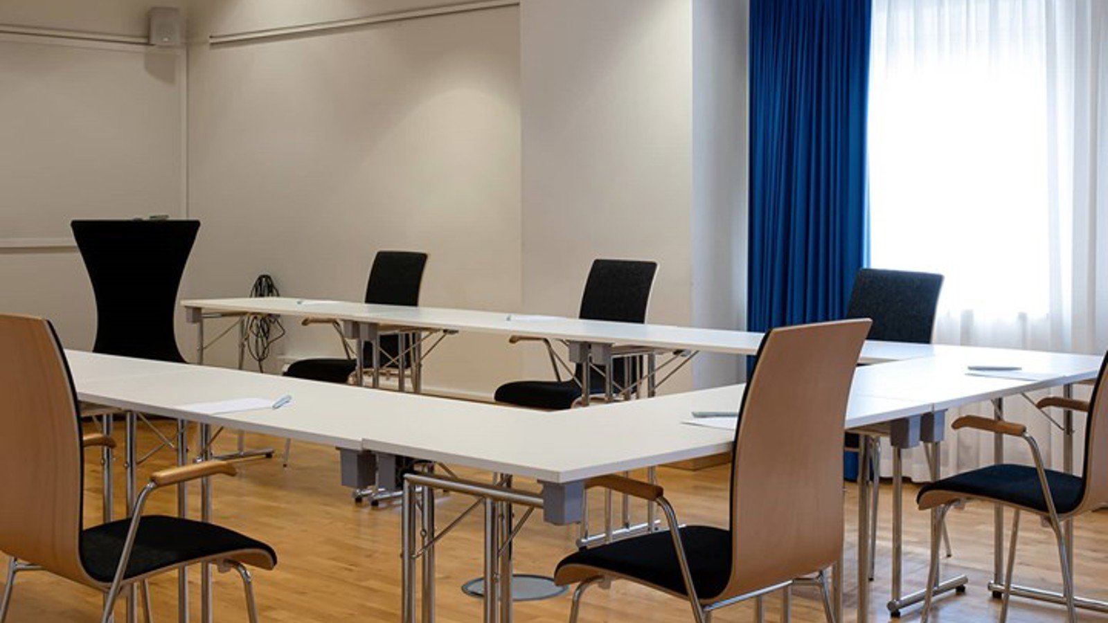 Konferensrum med u-sittning, vitt bord, parkett och blå gardiner