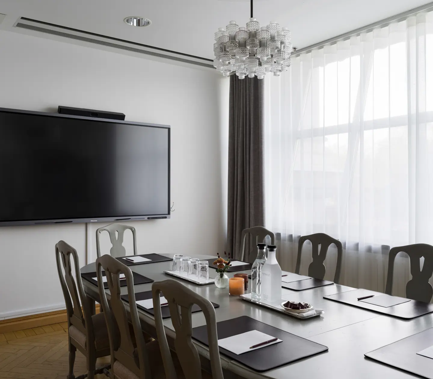 Modernt konferensrum med långbord, stolar, stor TV-skärm, anteckningsblock och vattenflaskor.
