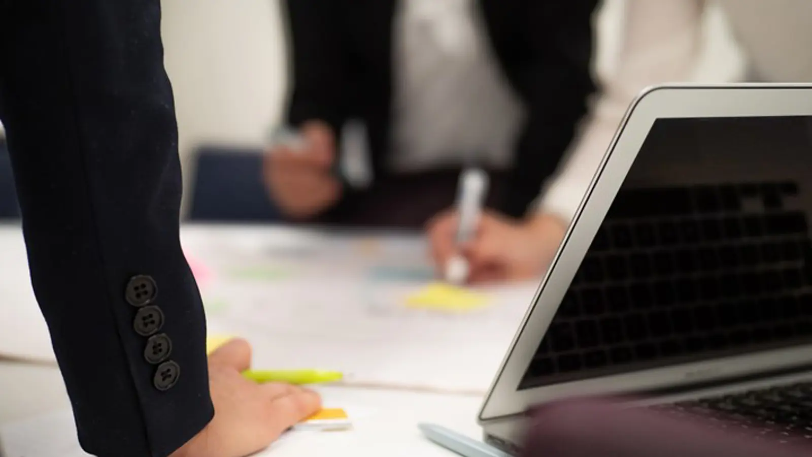 People leaning over conference table with pens in hands