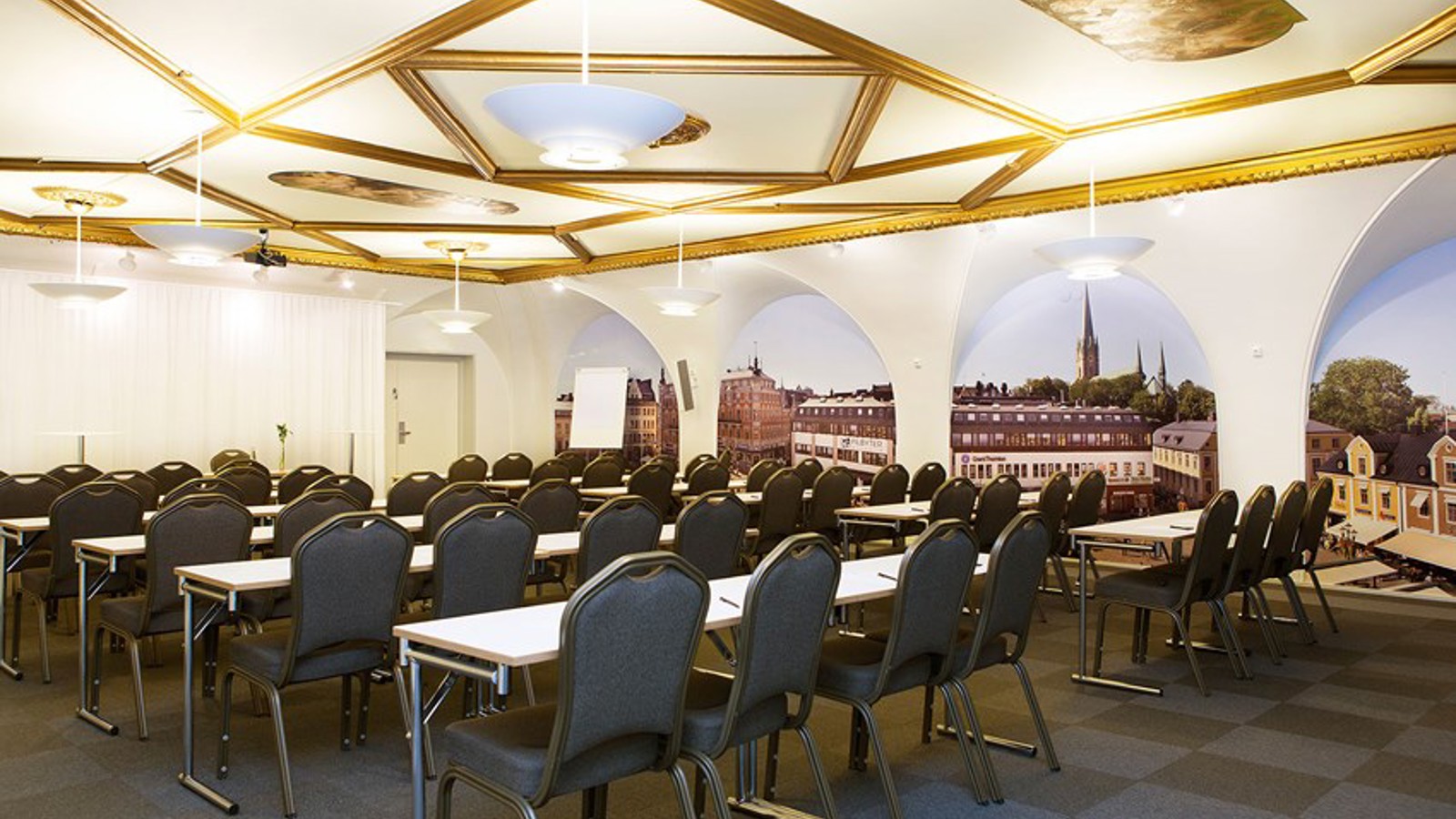 Stort konferensrum med skolsittning, upplyst tak med gulddetaljer och mörkt golv