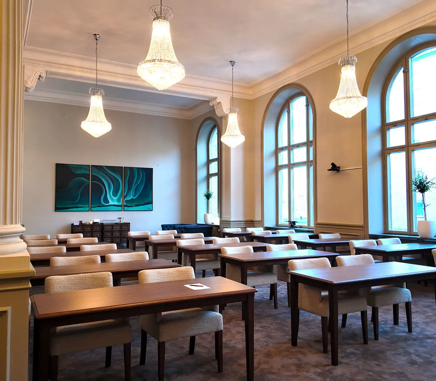 Elegant conference room with chandeliers, large arched windows, and rows of tables and chairs.