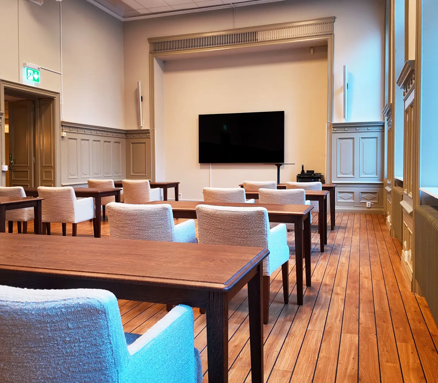 Modern conference room with wooden floors, upholstered chairs, and a large wall-mounted flat screen TV.