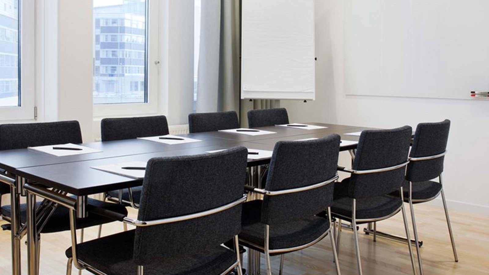 Konferensrum med styrelsesittning, brund bord, mörka stolar, vita väggar