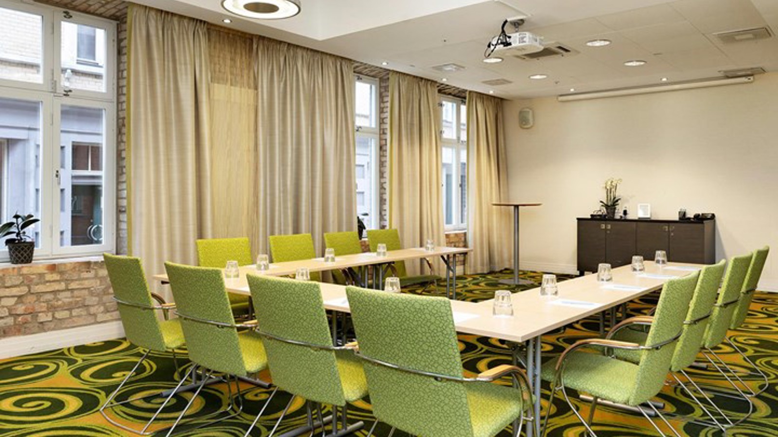 Konferensrum med u-sittning, gröna stolar, grönmönstrad matta och stora fönster