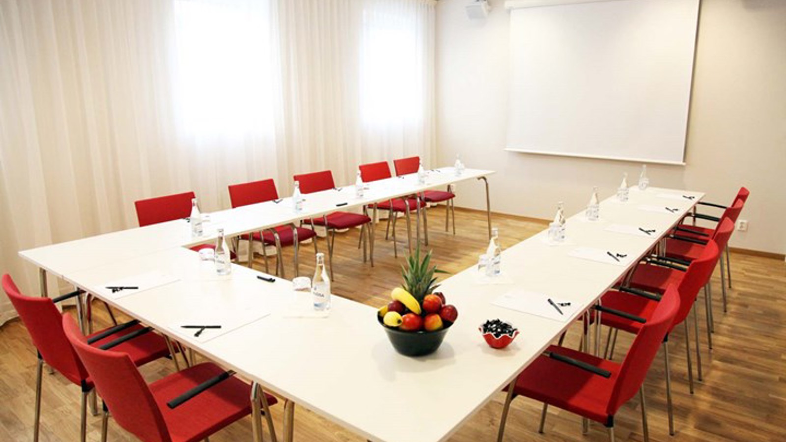 Konferensrum med u-sittning, vita väggar, vitt bord och röda stolar