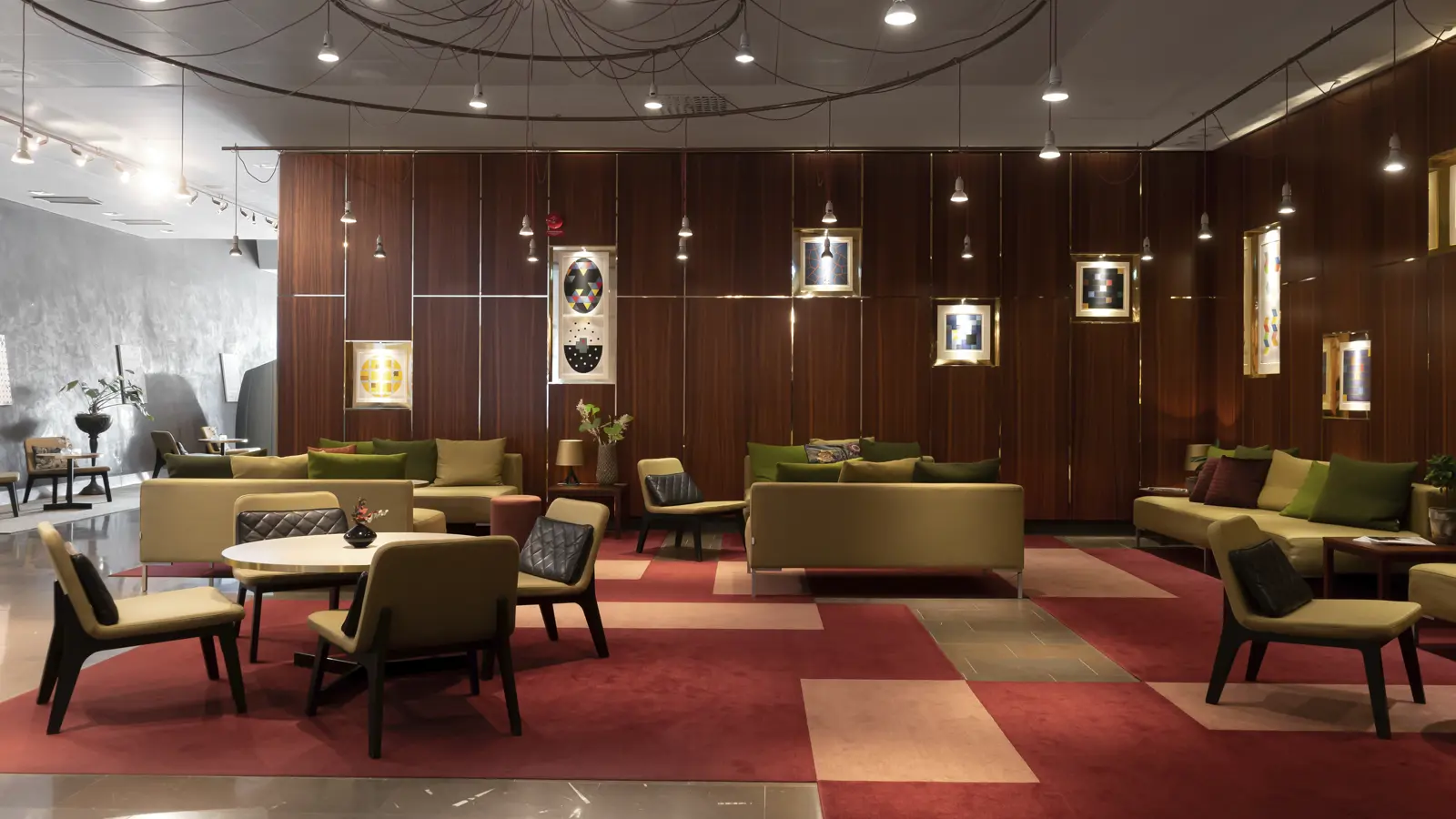 Modern hotel lobby with stylish seating, warm lighting, and contemporary decor, featuring plush sofas and armchairs against a wood-paneled wall with colorful framed artworks.