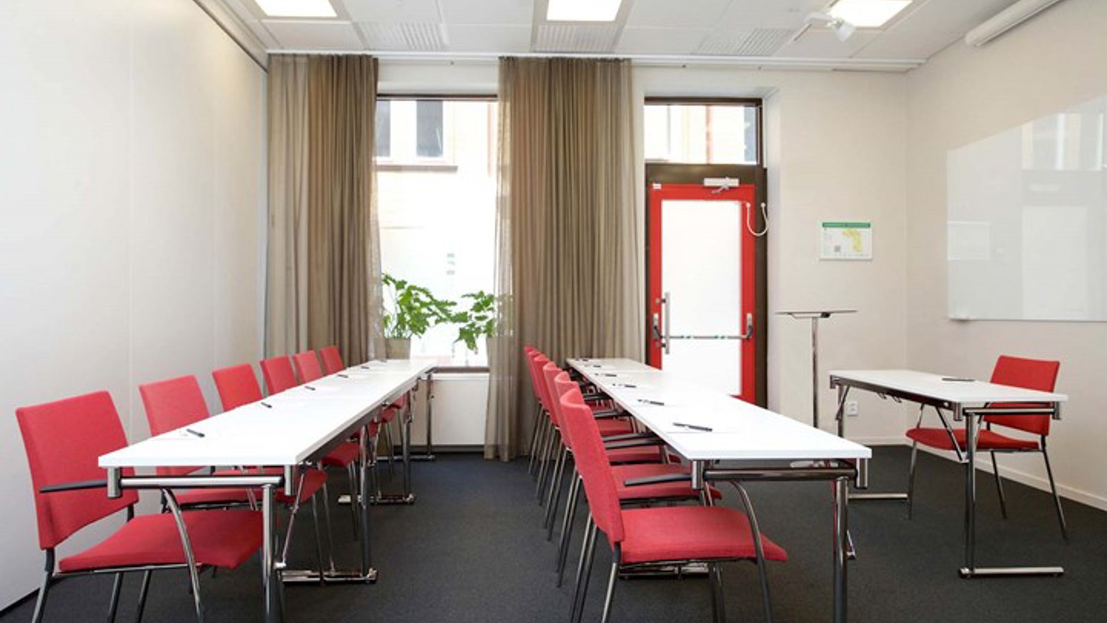 Konferensrum med skolsittning, vita bord, röda stolar och stort fönster