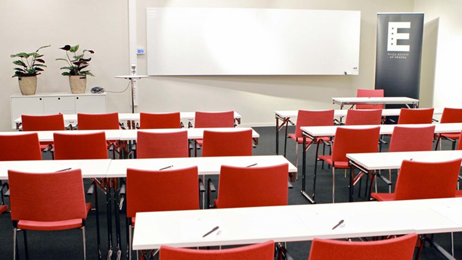 Konferensrum med skolsittning, vita bord, röda stolar