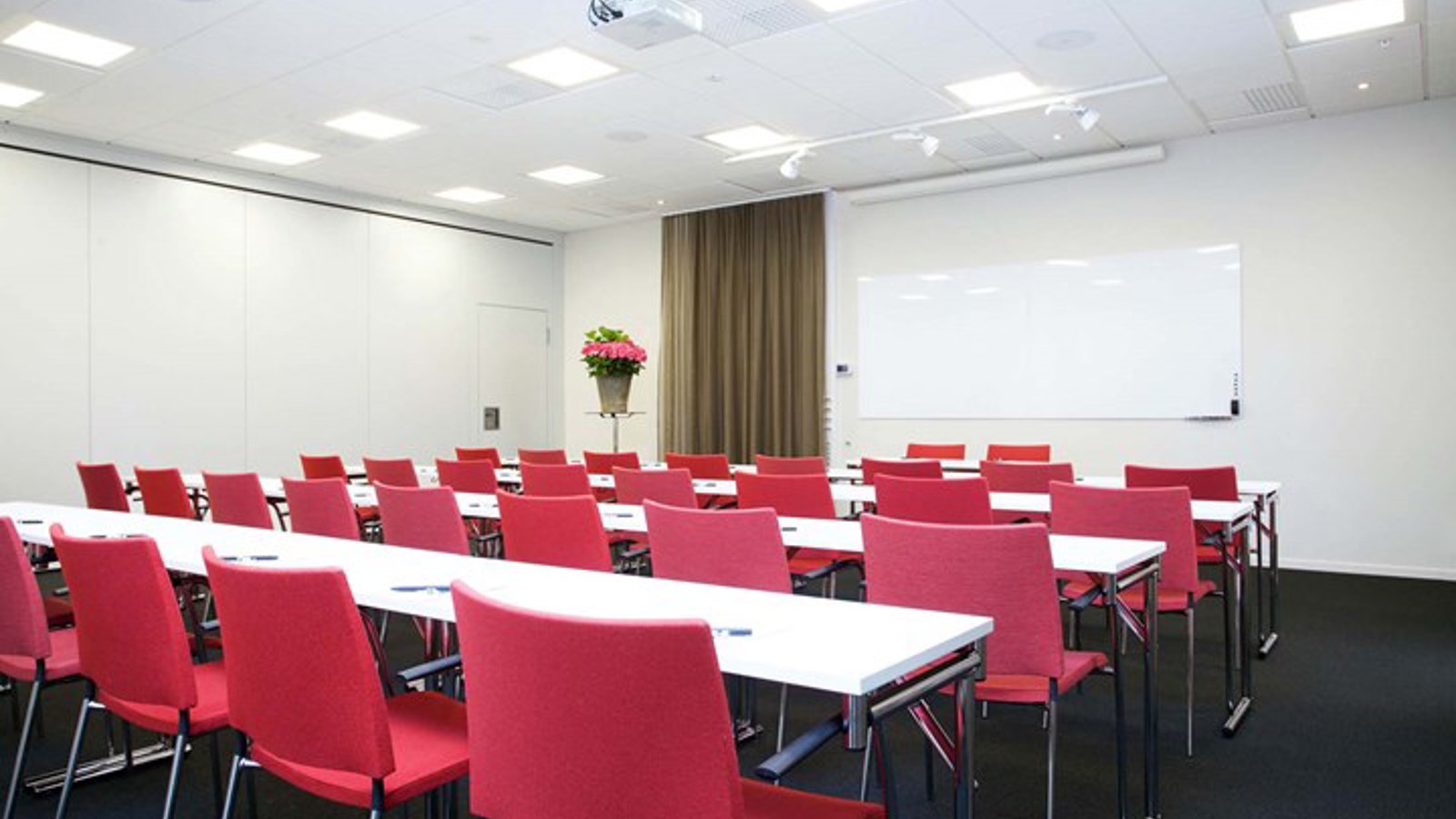 Konferensrum med vita bord, röda stolar, svart golv